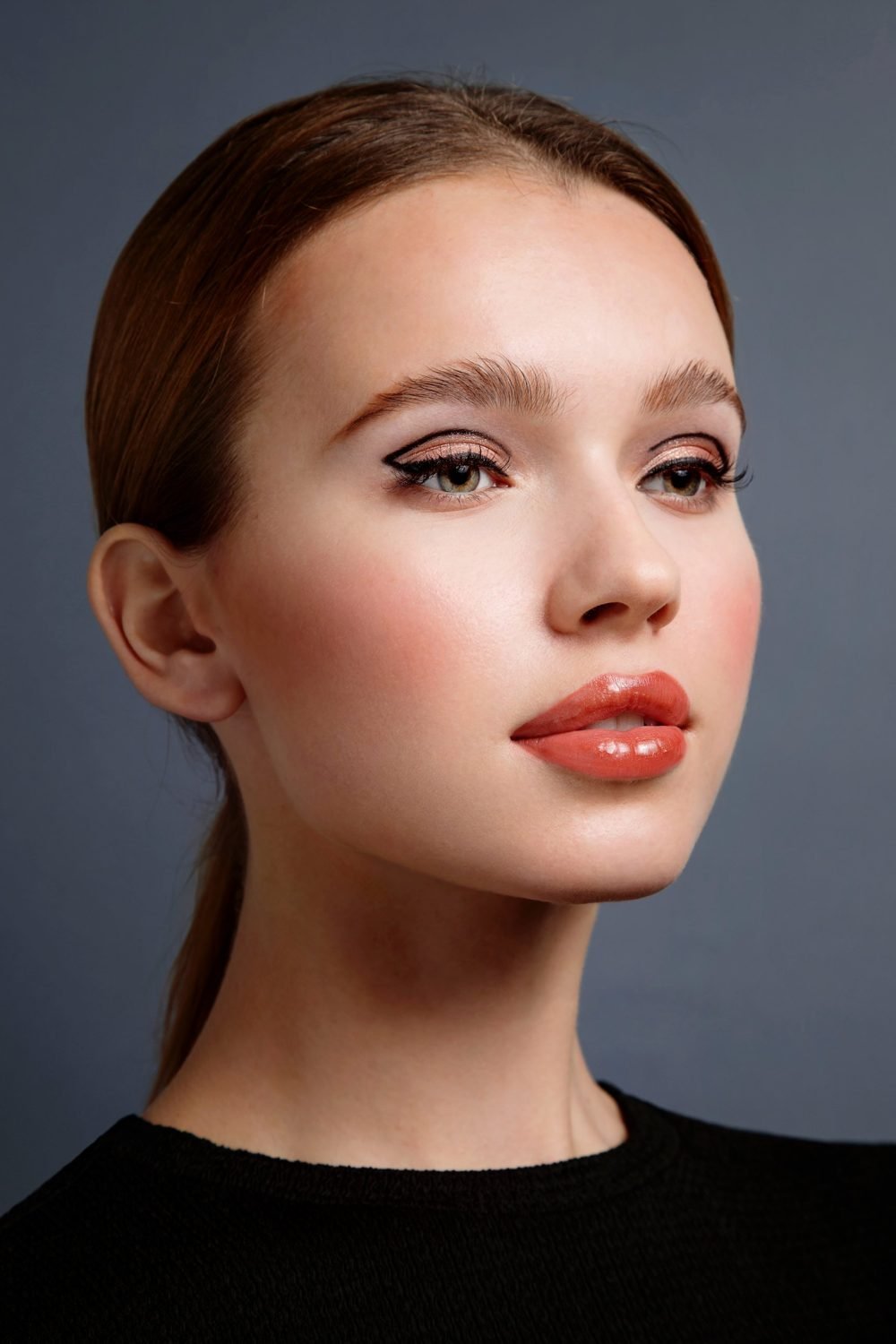Beauty portrait with graphic winged eyeliner, copper eyeshadow and glossy coral lips, grey backdrop