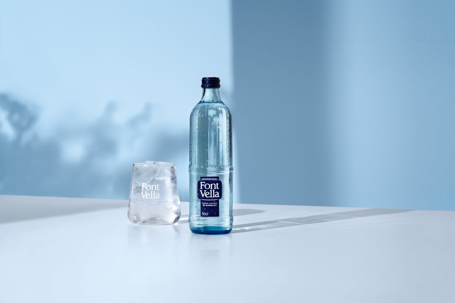Font Vella water bottle and glass on a blue background, after retouching
